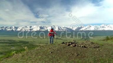 那个带着红色背包的旅行者的女人从山上站起来。 女人坐着，看着雪山，看着煤气